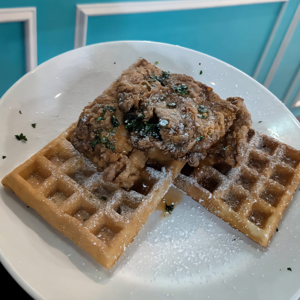 Chicken and waffles with powdered sugar and herbs on a white plate at Mornings on First.