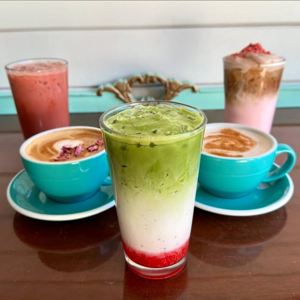 Assortment of colorful cafe drinks, including lattes and iced beverages, on a wooden table.