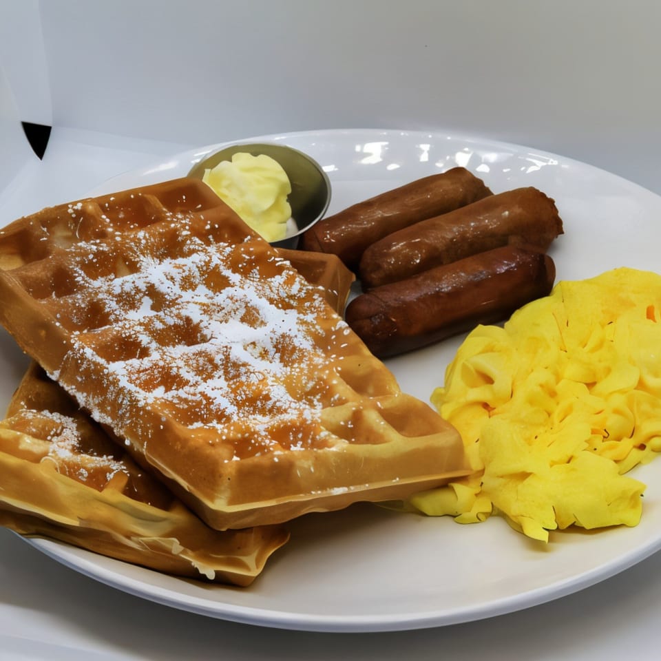 A breakfast plate with two powdered sugar waffles, scrambled eggs, and three sausage links.