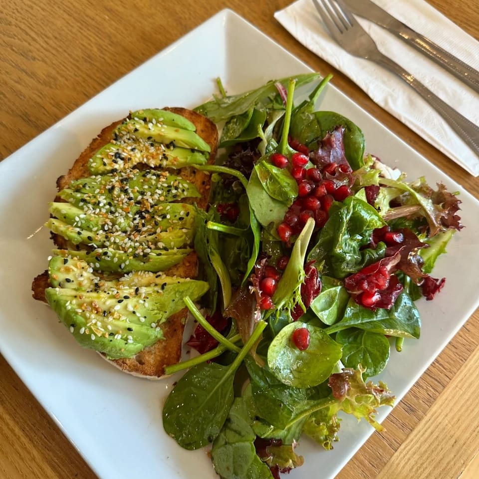 Avocado toast with everything bagel seasoning and a side salad with pomegranate seeds on a white plate.