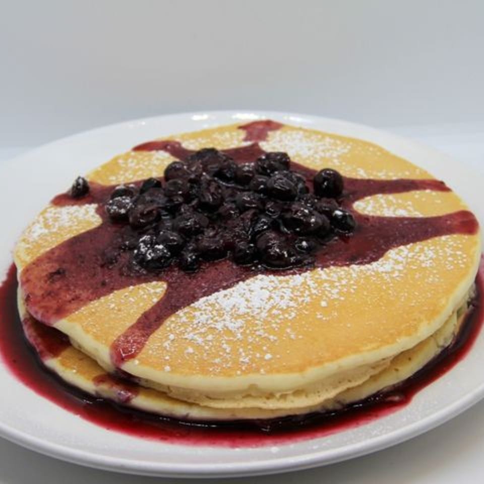 Fluffy pancakes topped with blueberry compote, powdered sugar, and berry syrup on a white plate.
